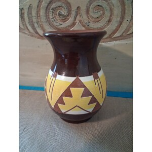 May include: A glossy dark brown ceramic vase featuring a wide, flared rim and a rounded body. The exterior is decorated with a repeating geometric pattern in yellow and white, consisting of triangular shapes and stylized angular lines.