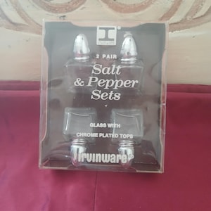 May include: A set of two glass salt and pepper shakers with chrome plated tops. The shakers are packaged in a clear plastic box with the text "2 pair Salt & Pepper Sets Glass with Chrome Plated Tops Irwinware" printed on the box.