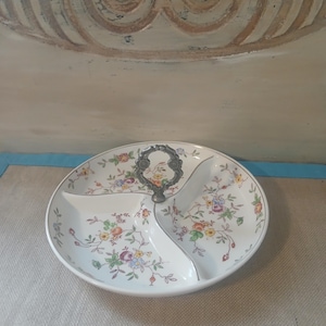May include: A white divided serving dish with a floral pattern in shades of pink, yellow, and blue. The dish has a silver handle and a gray trim. The dish is round and has three sections.