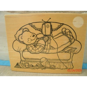 May include: A wooden stamp featuring a cartoon bear relaxing on a couch, watching TV. The bear is wearing a plaid shirt and boots. The stamp includes text that reads "BEARLY SPORTS NEWS" and "01/24/2026".