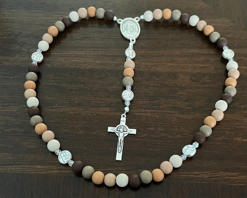 May include: A brown, beige and white wooden bead rosary with a silver crucifix and silver medallions.