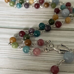 May include: A colorful rosary with a silver charm of the Virgin Mary. The beads are made of various shades of blue, green, brown, pink, and yellow.