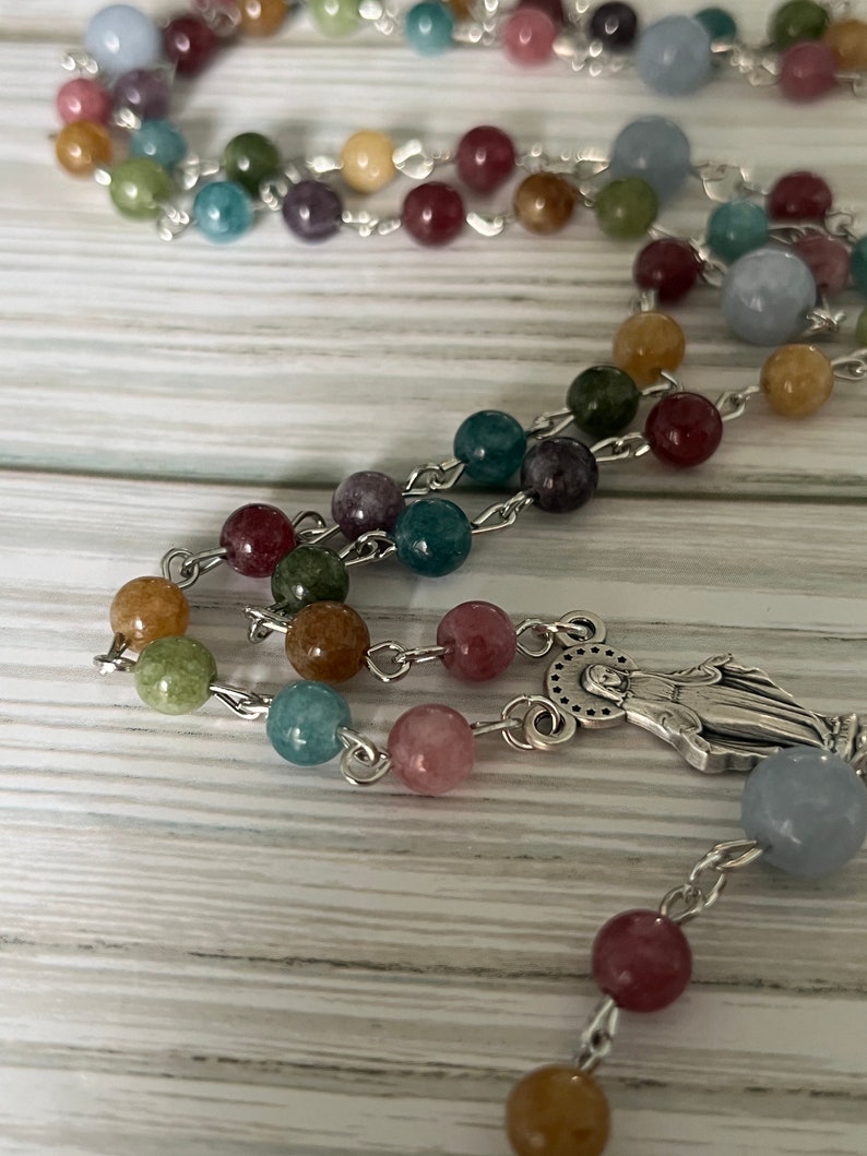 May include: A colorful rosary with a silver charm of the Virgin Mary. The beads are made of various shades of blue, green, brown, pink, and yellow.