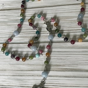 May include: A multi-colored rosary with a silver crucifix and a silver charm of the Virgin Mary. The beads are made of various shades of blue, green, brown, and pink.
