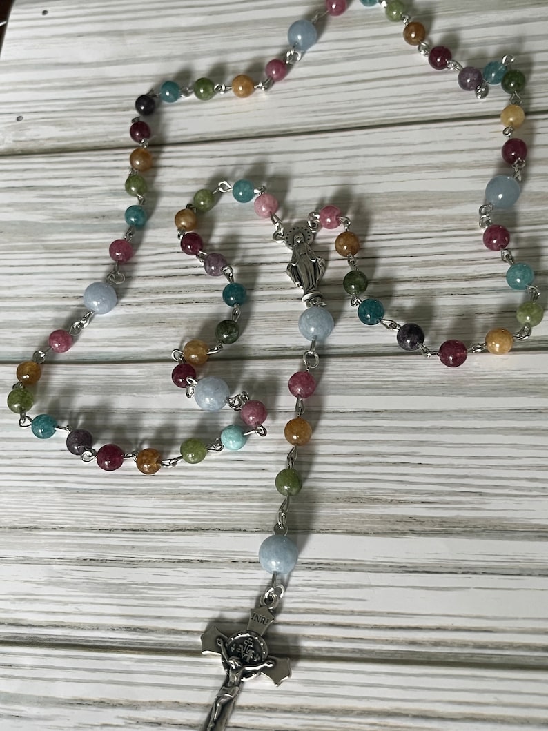 May include: A multi-colored rosary with a silver crucifix and a silver charm of the Virgin Mary. The beads are made of various shades of blue, green, brown, and pink.