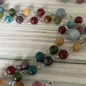 May include: A colorful beaded rosary with a silver chain and a silver pendant featuring a depiction of the Virgin Mary.