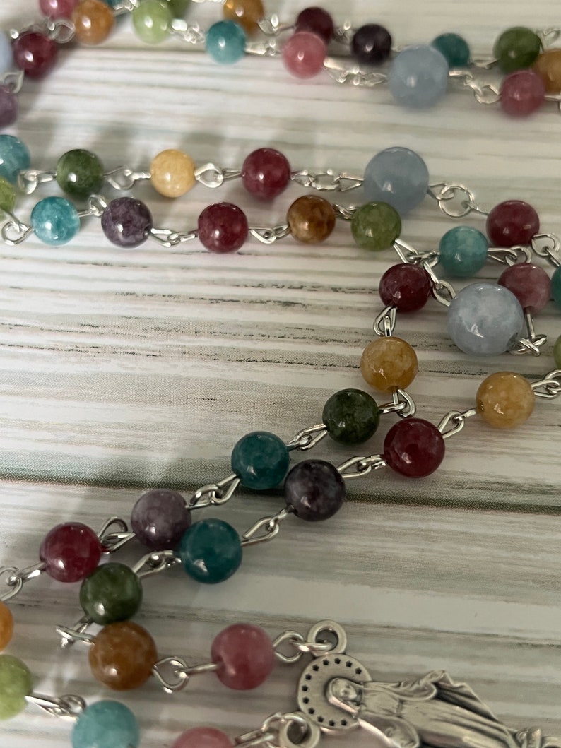 May include: A colorful beaded rosary with a silver chain and a silver pendant featuring a depiction of the Virgin Mary.