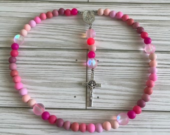 May include: A pink and white rosary with iridescent beads and a silver crucifix and a silver charm of the Virgin Mary.