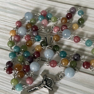 May include: A colorful rosary with a silver crucifix and a silver charm of the Virgin Mary. The beads are made of various shades of blue, green, brown, and pink.