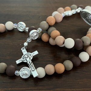 May include: Two brown and beige beaded rosaries with silver accents. The rosaries have a silver crucifix and a silver medal with a religious image.