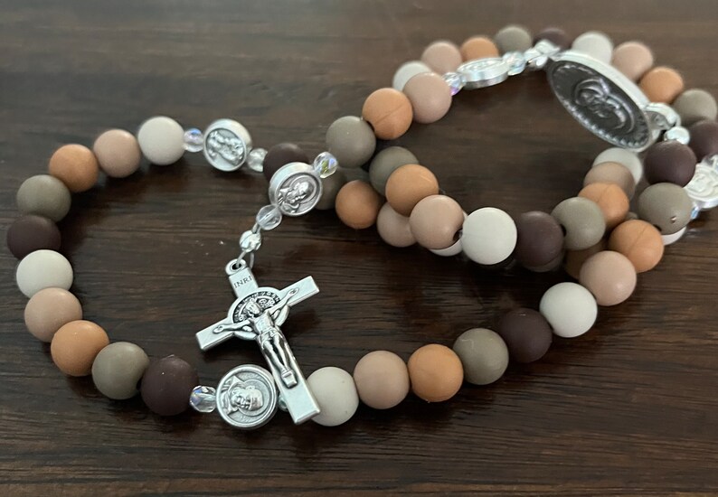 May include: Two brown and beige beaded rosaries with silver accents. The rosaries have a silver crucifix and a silver medal with a religious image.