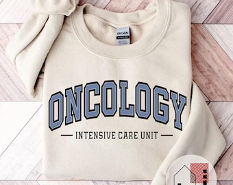 May include: A beige sweatshirt with the text "ONCOLOGY - INTENSIVE CARE UNIT -" in blue and black lettering.