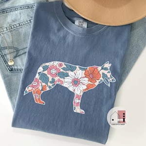Pu&ograve; includere: Una maglietta blu con un motivo floreale a forma di cane. Il motivo floreale &egrave; in tonalit&agrave; di rosa, arancione e blu. La maglietta ha l'etichetta "Company Colors".