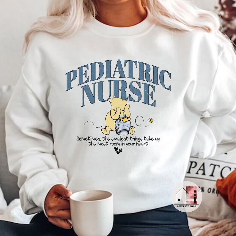 May include: White sweatshirt with blue text that reads "Pediatric Nurse" and a cartoon Winnie the Pooh holding a honey pot. The text below the image reads "Sometimes, the smallest things take up the most room in your heart."