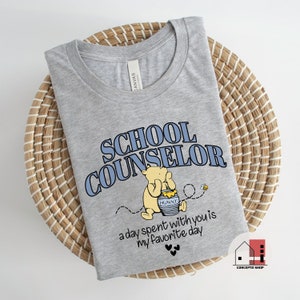 May include: Gray t-shirt with a Winnie the Pooh illustration and the text "School Counselor" in blue. The text "a day spent with you is my favorite day" is printed below the illustration.