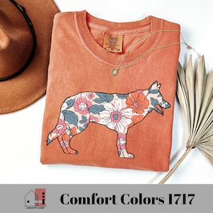Pu&ograve; includere: Una maglietta color terracotta con una stampa floreale di un pastore tedesco. La maglietta ha il testo "Comfort Colors" stampato sull'etichetta.