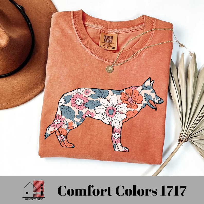 Pu&ograve; includere: Una maglietta color terracotta con una stampa floreale di un pastore tedesco. La maglietta ha il testo "Comfort Colors" stampato sull'etichetta.