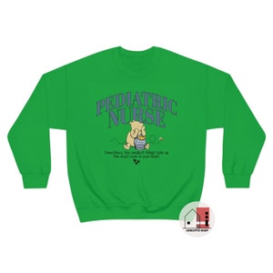 May include: Green sweatshirt with the text "PEDIATRIC NURSE" in blue and white lettering. A cartoon Winnie the Pooh character is holding a honey pot. The text "Sometimes, the smallest things take up the most room in your heart" is below the image.