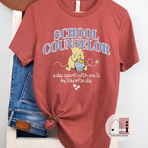 May include: A red t-shirt with the text "SCHOOL COUNSELOR" in blue letters. A cartoon bear with a honey pot is pictured below the text. The text "a day spent with you is my favorite day" is below the bear.
