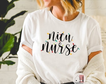 May include: White t-shirt with the words "NICU Nurse" in black script, adorned with colorful string lights. The shirt is a crew neck style and appears to be made of a soft material. The design is centered on the front of the shirt.