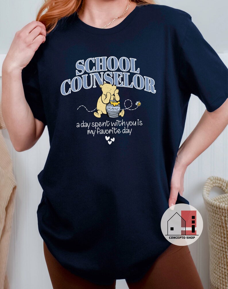 May include: Navy blue t-shirt with the text "School Counselor" in white and blue lettering. A cartoon Winnie the Pooh bear is holding a jar of honey with the text "Hunny" on it. The text "a day spent with you is my favorite day" is below the bear.