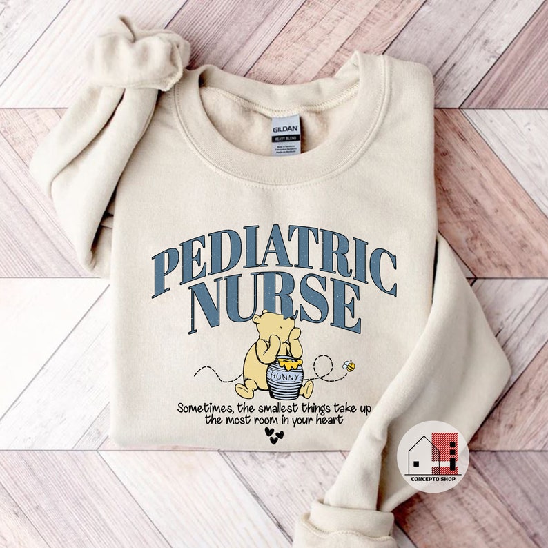 May include: A beige sweatshirt with the text "PEDIATRIC NURSE" in blue lettering. A cartoon Winnie the Pooh character is holding a jar of honey with the text "HUNNY" on it. The text "Sometimes, the smallest things take up the most room in your heart" is below the image.