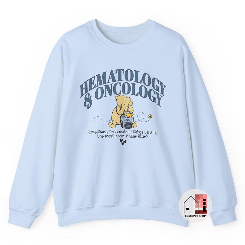 May include: A light blue sweatshirt featuring the text "HEMATOLOGY & ONCOLOGY" above a cartoon illustration of Winnie the Pooh with a honey pot. The text "Sometimes, the smallest things take up the most room in your heart" is below the illustration.