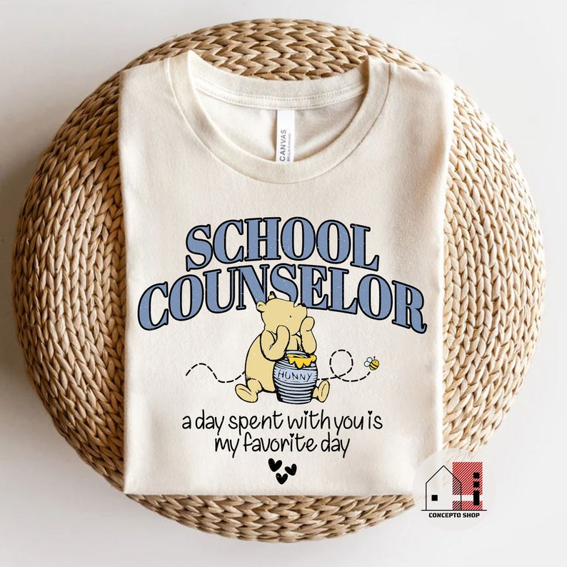 May include: A beige t-shirt with the text "SCHOOL COUNSELOR" in blue letters. A cartoon Winnie the Pooh character is sitting on a pot of honey with a bee flying nearby. The text "a day spent with you is my favorite day" is below the image.