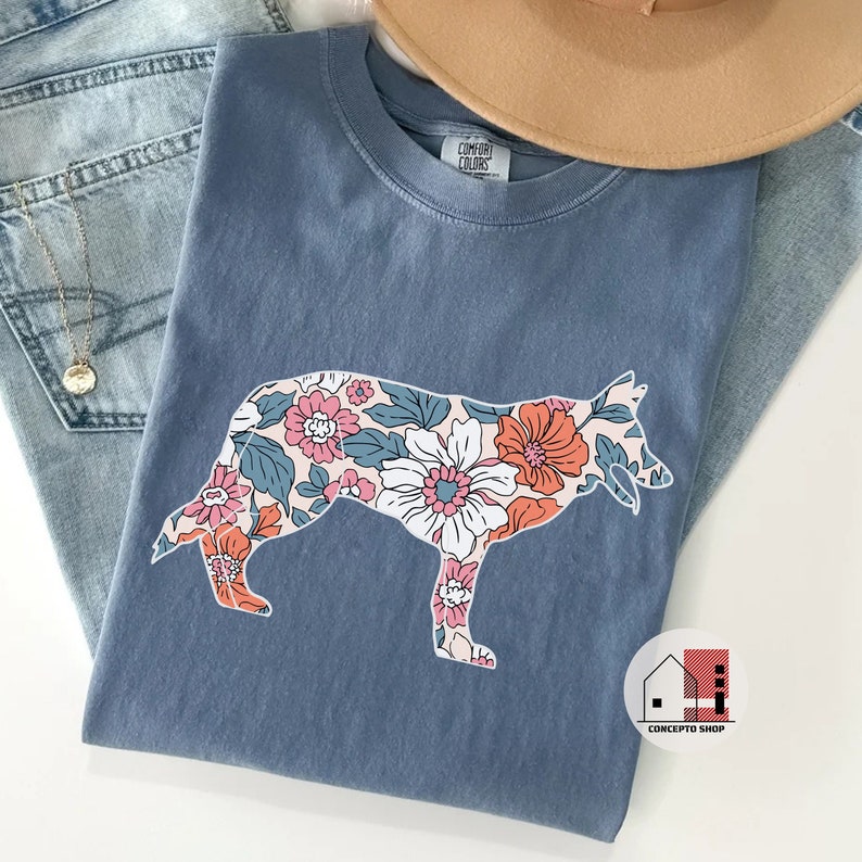 Pu&ograve; includere: Una maglietta blu con un motivo floreale a forma di cane. Il motivo floreale &egrave; in tonalit&agrave; di rosa, arancione e blu. La maglietta ha l'etichetta "Company Colors".