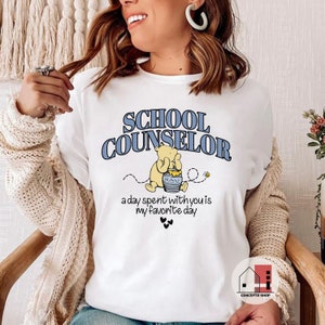 May include: White t-shirt with a blue and white graphic of Winnie the Pooh holding a honey pot. The text "School Counselor" is above the graphic and "a day spent with you is my favorite day" is below the graphic.