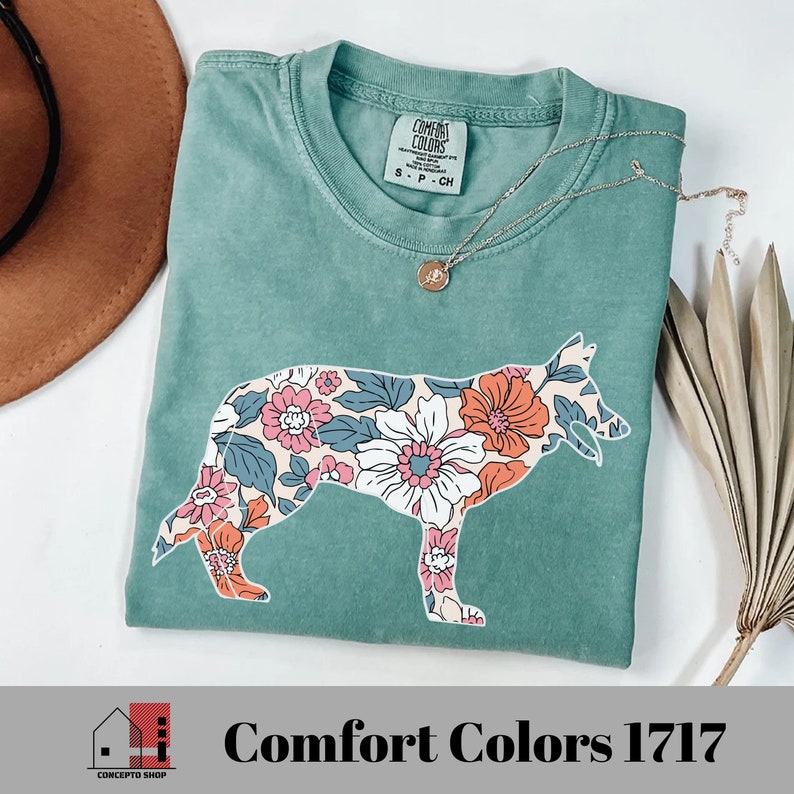 Pu&ograve; includere: Una maglietta blu turchese con una stampa floreale a forma di silhouette di pastore tedesco. La maglietta ha il testo "Comfort Colors" e "1717" stampato sull'etichetta.