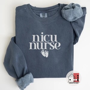 May include: A dark blue sweatshirt with the text "nicu nurse" in white lettering and a pair of white footprints below the text.