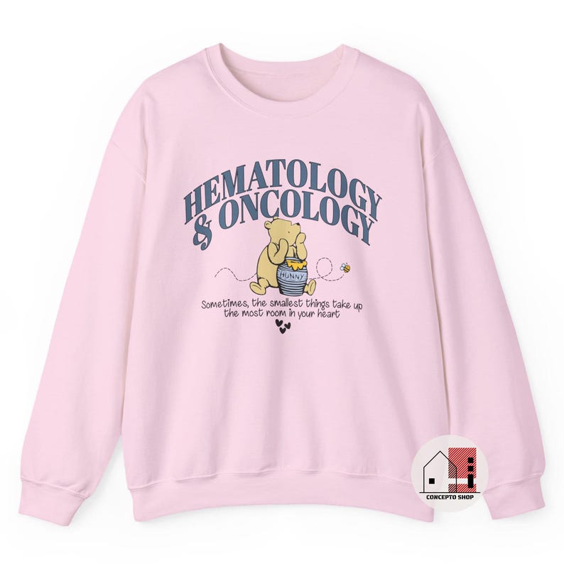 May include: A light pink sweatshirt featuring a graphic of Winnie the Pooh holding a honey pot, with the text "HEMATOLOGY & ONCOLOGY". Below the graphic is the text "Sometimes, the smallest things take up the most room in your heart."