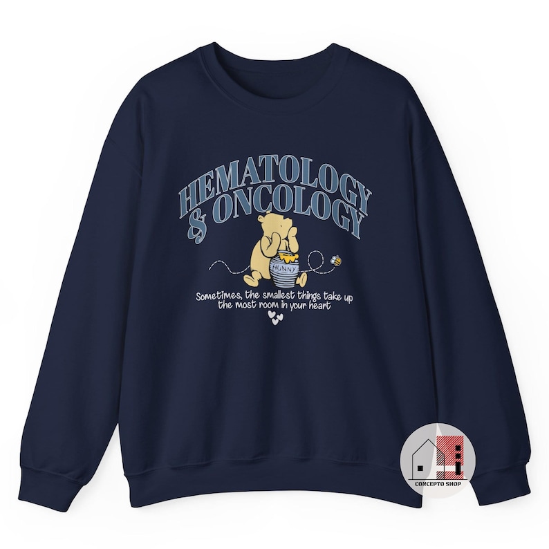 May include: Navy blue sweatshirt featuring a graphic of Winnie the Pooh holding a honey pot, with the words "HEMATOLOGY & ONCOLOGY" above and a quote below. The design includes bees and hearts.