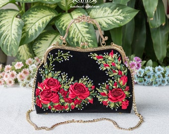 May include: A black velvet handbag with a gold chain strap and a gold clasp. The bag is decorated with red ribbon embroidery of roses and leaves.
