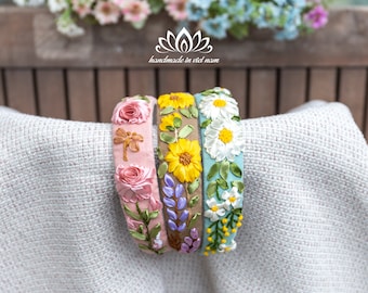May include: Three handmade headbands with embroidered floral designs. The headbands are in shades of pink, yellow, and blue. The text "handmade in viet nam" is visible in the image.