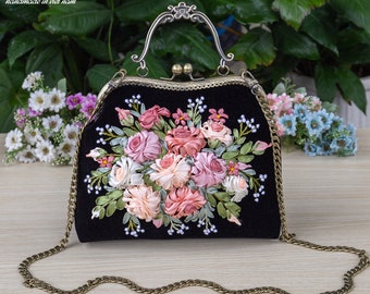 以下が含まれることがあります： 花柄の刺繍が施された黒いベルベット製のハンドバッグ。バッグにはトップハンドルとチェーンストラップが付いています。刺繍にはピンク、白、緑のリボンローズが施されています。