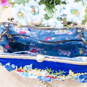 May include: A blue velvet clutch purse with a floral design and a gold chain strap. The purse is open and the inside is lined with a blue and white floral fabric.
