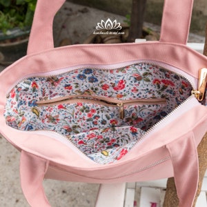 K&ouml;nnte beinhalten: Eine rosa Canvas-Tragetasche mit einem floralen Futter. Die Tasche hat einen Rei&szlig;verschluss und eine kleine Rei&szlig;verschlusstasche im Inneren. Die Tasche ist handgefertigt in Vietnam.