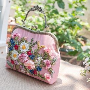 May include: A pink satin clutch bag with a floral embroidery design. The embroidery features pink, white, blue, and green ribbon flowers.