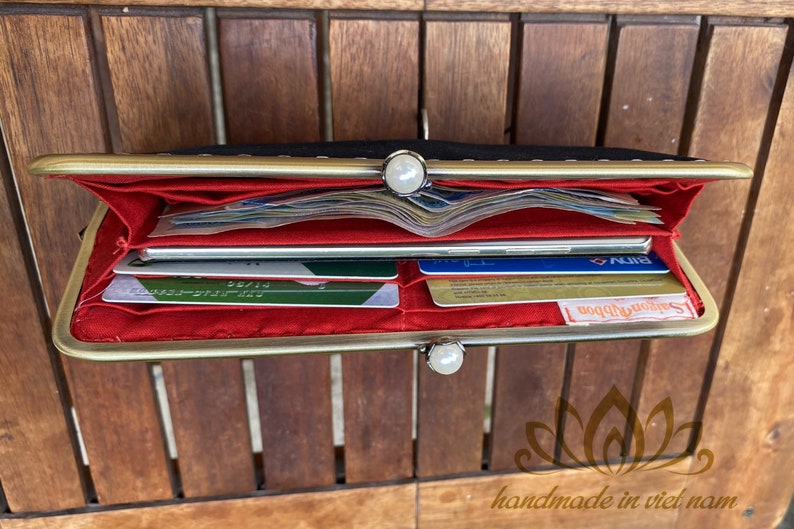 Op de afbeelding: Een zwarte leren portemonnee met een gouden metalen frame en een rode voering. De portemonnee is open en toont meerdere creditcards en contant geld van binnen.