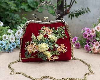 Può includere: Una borsetta di velluto rosso con un design floreale ricamato con nastro. La borsa ha una tracolla a catena dorata e una chiusura dorata.