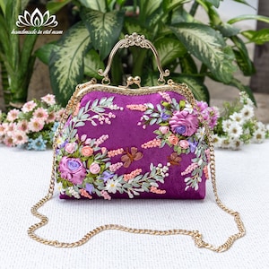 May include: A purple velvet handbag with a gold chain strap and intricate floral embroidery. The embroidery features pink, white, and green silk ribbon flowers.