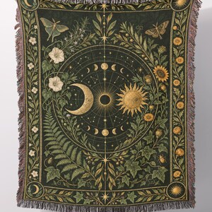 May include: A rectangular woven throw blanket featuring a dark green background with a central celestial design of a sun and moon surrounded by lunar phases, moths, sunflowers, ferns, and botanical elements with fringed edges on all sides.