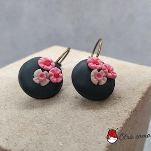 May include: A pair of black and pink floral earrings. The earrings are made of polymer clay and have a simple, round shape. The flowers are pink with white centres.
