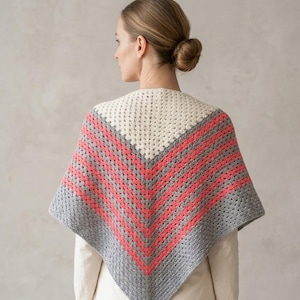 Puede incluir: Un chal de ganchillo hecho a mano con un diseño en forma de V. El chal presenta una sección superior de color crema, seguida de rayas alternas de coral y gris. El borde inferior es gris. El chal se lleva sobre una parte superior de color crema.