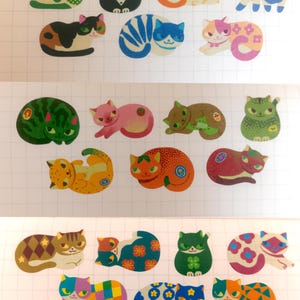 May include: A collection of twenty-three individual cat stickers arranged in three rows on a white grid background. Each sticker features a unique cat illustration with various colors, patterns, and poses, including solid, spotted, and floral designs.