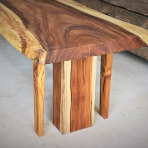 May include: A wooden bench with a natural live edge top and four legs. The bench is made of light and dark brown wood.