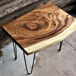 May include: A wooden side table with a live edge top and black hairpin legs. The wood grain is visible and has a natural, rustic look.