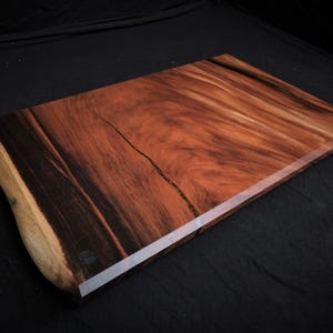 May include: A large, rectangular wooden cutting board with a natural edge and a dark brown wood grain. The board has a clear epoxy finish.